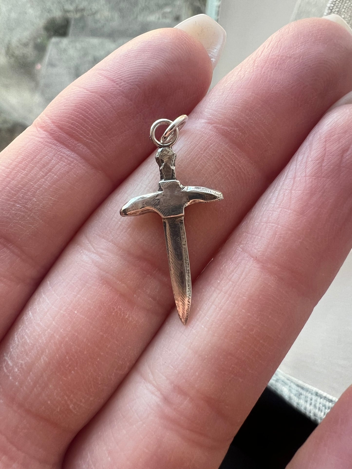 Small metal sword pendant held between fingers